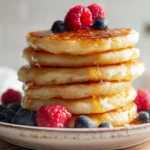 Stack of fluffy cottage cheese pancakes with berries and syrup