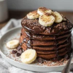 Chocolate protein pancakes stacked with bananas and a drizzle of dark chocolate