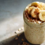 A glass jar filled with creamy cottage cheese overnight oats topped with banana slices and cinnamon