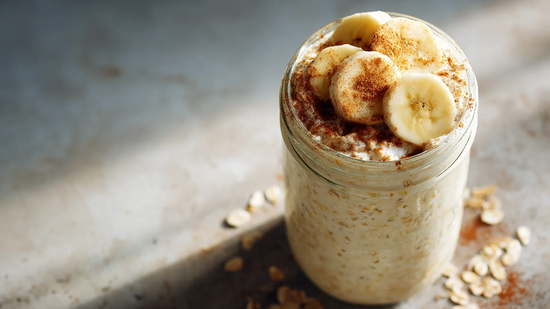 A glass jar filled with creamy cottage cheese overnight oats topped with banana slices and cinnamon