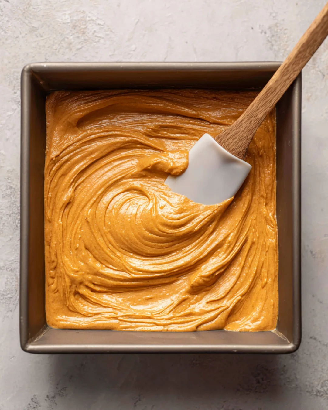 Pumpkin cheesecake filling being smoothed over crust in a pan.
