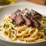 Creamy garlic parmesan steak pasta served in a white bowl with garnishes.